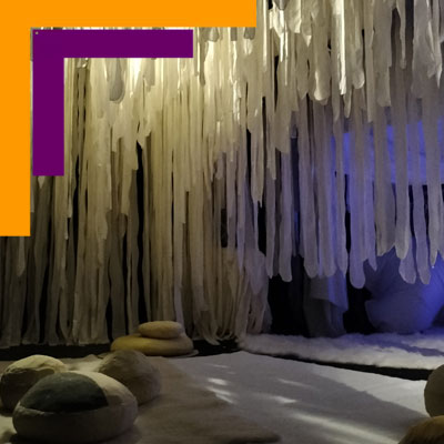 Visuel du spectacle "émouvoir". On voit un décor qui ressemble à des stalactites éclairées par des lmières douces, et des coussins pour accueillir les jeunes spectateurs.