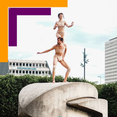 Visuel du spectacle Obake. On voit deux acrobates perchés sur une sculpture urbaine, la fille sur les épaules du garçon.