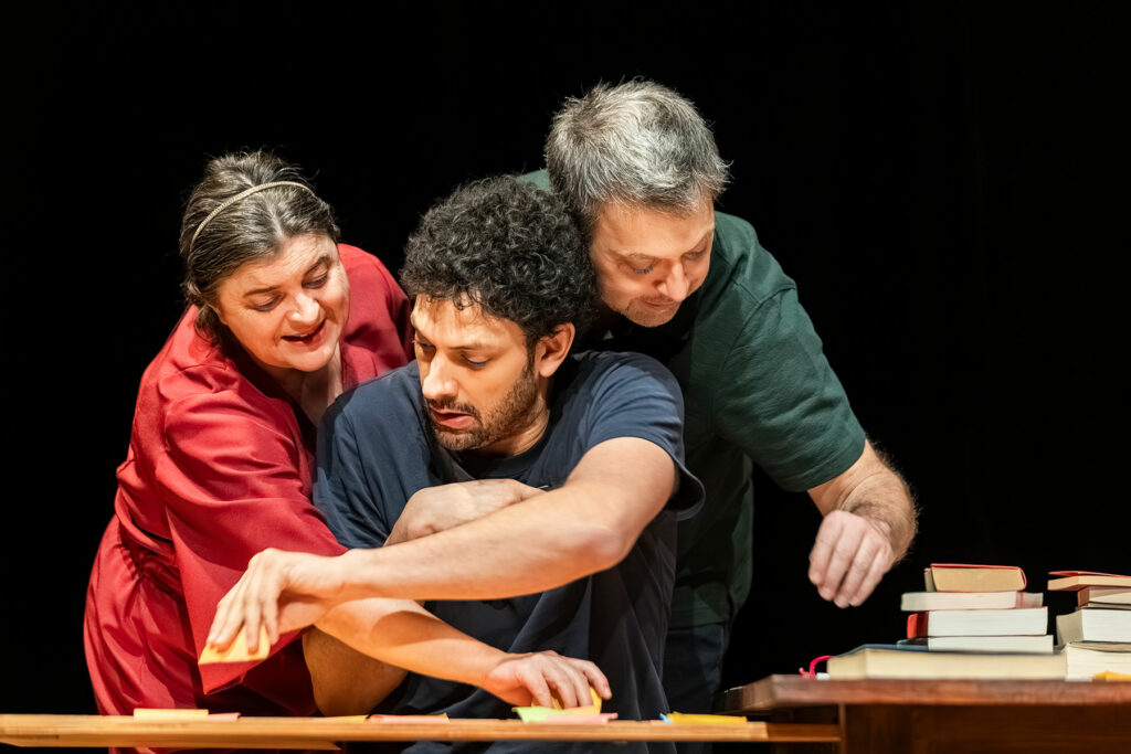 Le visuel illustre le spectacle "On n'est pas assez nombreux pour jouer Shakespeare". On voit 2 hommes et une femme, penchés sur une table jonchée de livres, qui semblent très occupés à classer, trier, évaluer.