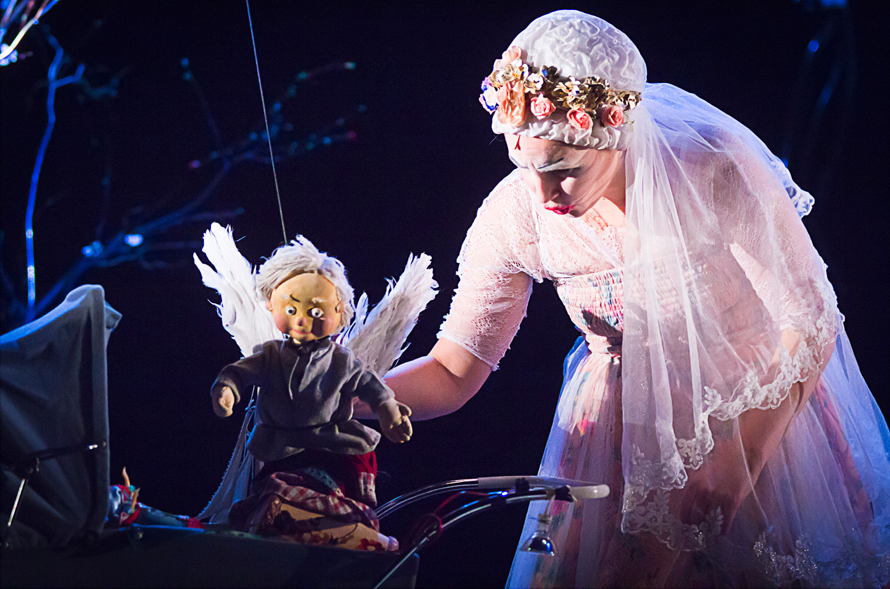 Le visuel illustre le spectacle "Les enfants c'est moi". Il montre une femme clown, vêtue en mariée, penchée sur un berceau avec à la main une marionnette d'ange.