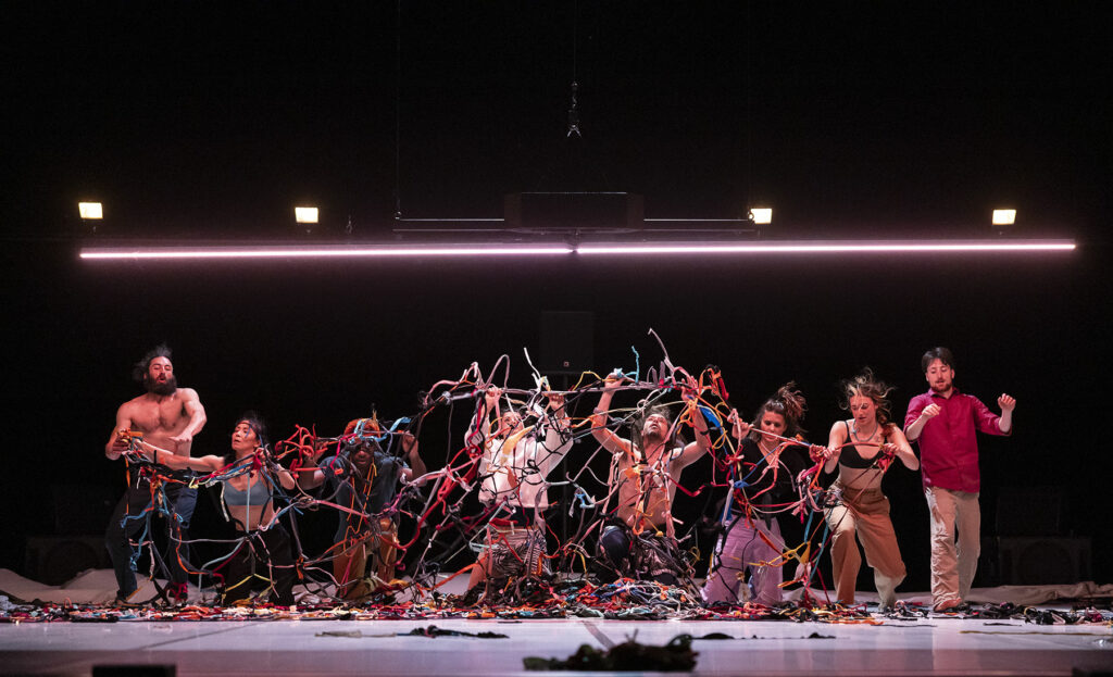 Le visuel du spectacle de danse "De loin si près" représente des danseurs contemporains vêtus de teeshirts colorés qui brandissent des bandelettes de couleur qu'ils assemblent entre elles à la manière d'un filet.