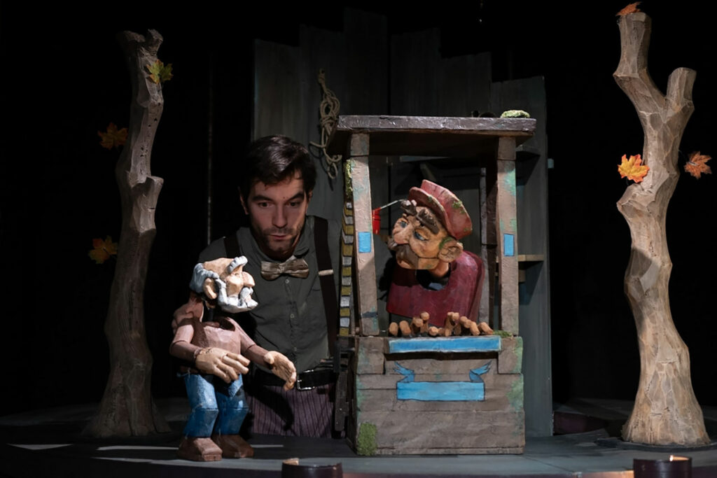 La photo du spectacle montre un petit carrousel sur lequel est posé un guichet dans lequel se trouve une marionnette masculine avec sa casquette. Ik parle avec un vieux monsieur, marionnette lui aussi, debout au pied d'un arbre en papier mâché